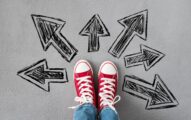 Feet in sneakers on the road with painted arrows pointing to different ways