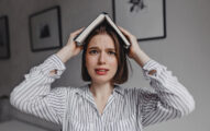 Brown-eyed girl puts book on her head, looking at camera bewildered and frightened.