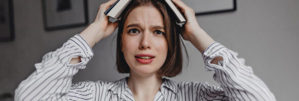 Brown-eyed girl puts book on her head, looking at camera bewildered and frightened.