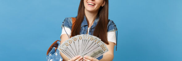 Portrait of young smiling attractive woman student in denim clothes with backpack holding lots of dollars