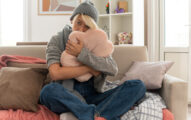 Person hugging a pink pillow on a couch, looking sad.